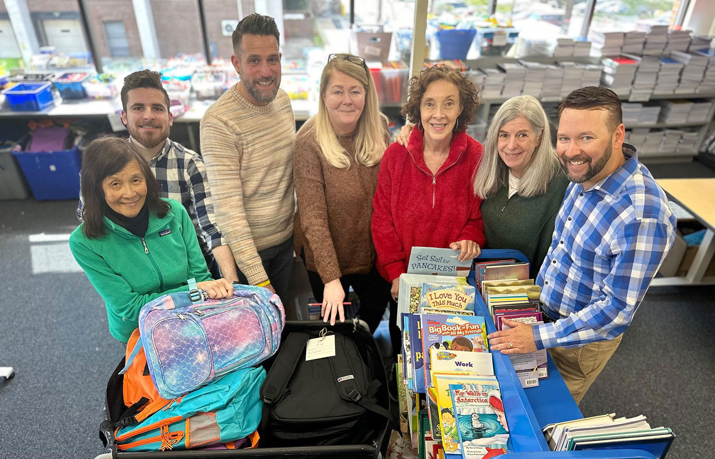 A-group-of-men-and-women-surround-piles-of-books-and-bookbags-in-a-library-setting