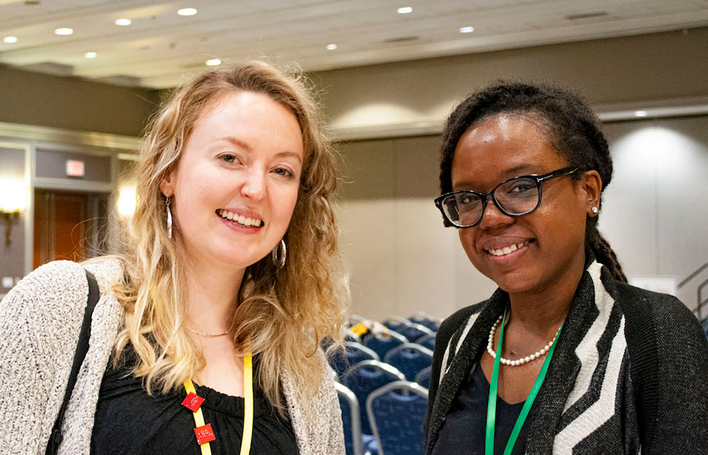 A-white-woman-and-black-woman-wearing-cardigans-in-an-event-setting-smiling