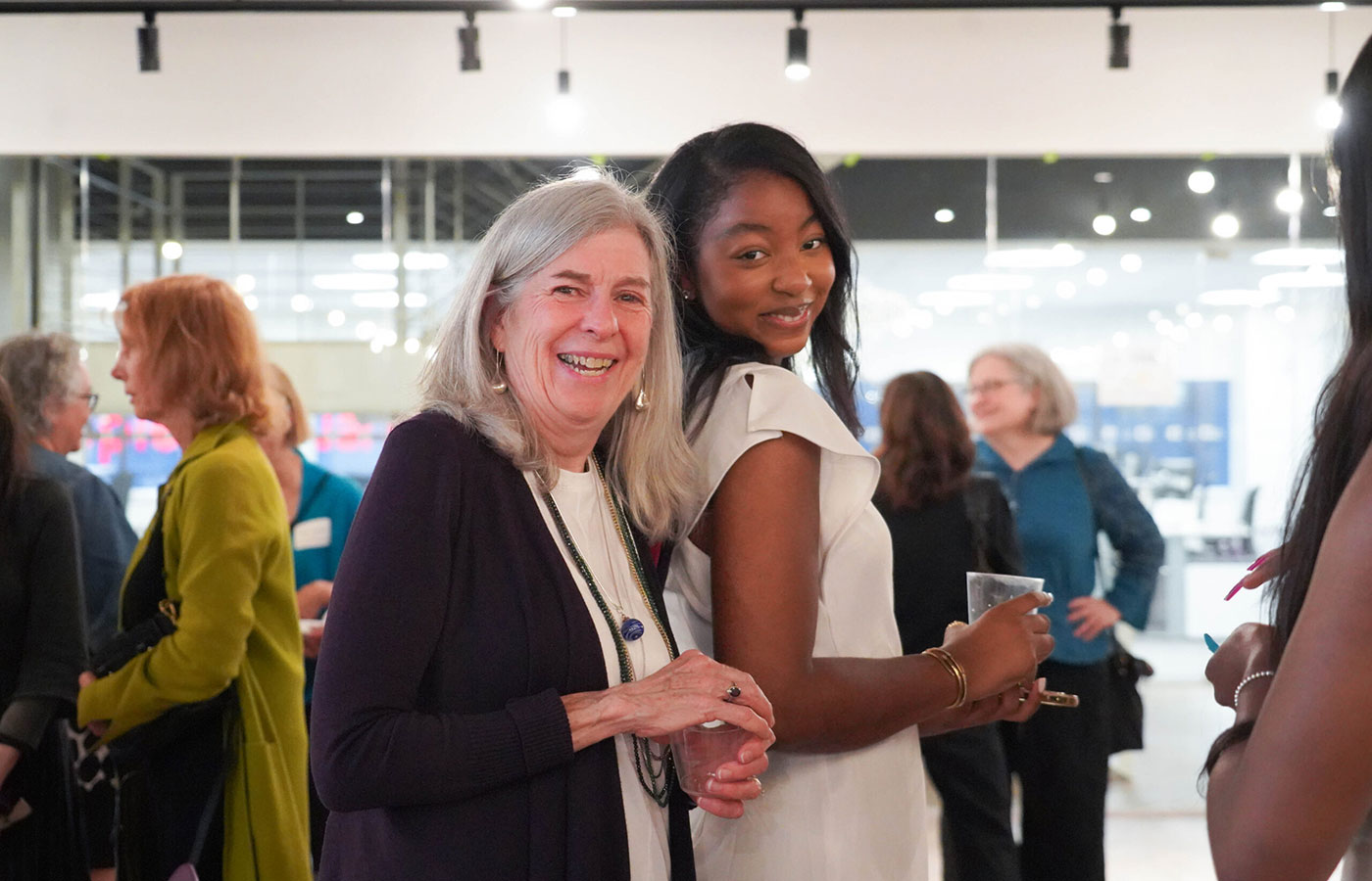 Smiling-white-lady-with-gray-hair-stands-beside-a-young-smiling-Black-woman-at-an-event